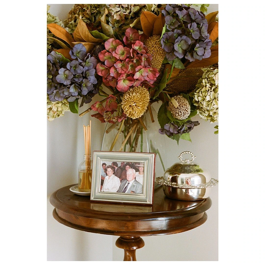 Bob - 2021 — Flowers above a framed family photograph on a small table